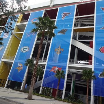Oversized 9 oz heavy duty mesh banners on the side of a large building, printed with various NFL logos.